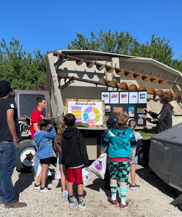 Group leader Ben Rogers (wearing red) takes his group of elementary students to the almond station, where station leaders Dilawar Singh (left) and Trent Olmo (right) talk about the process of growing and harvesting almonds.