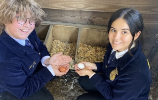 Chapter Reporter and Student Advisor, Kacey and Aiden, collect eggs.