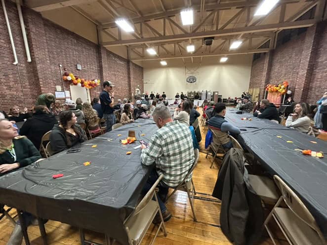 Community members and supporters sit at tables, with FFA members in the background.