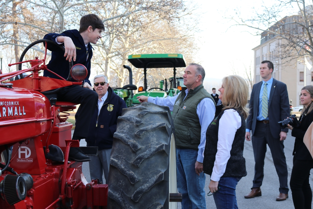 Director Chris Chinn, Govenor Mike Kehoe and Former Governor Mike Parson talk to an FFA member at the “Drive Your Tractor to Work Day” event.