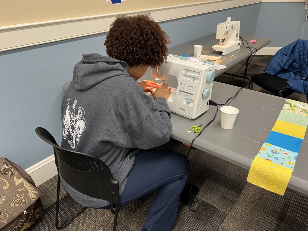 Volunteers utilize donated sewing machines to piece squares together.