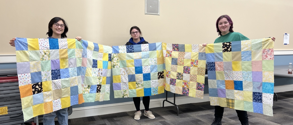 Norfolk FFA Chapter President Miru Kunst (left), Vice President Gabriella Pannon (middle) and Junior Parliamentarian Jaxon Sennott (right) hold a few completed quilt tops.